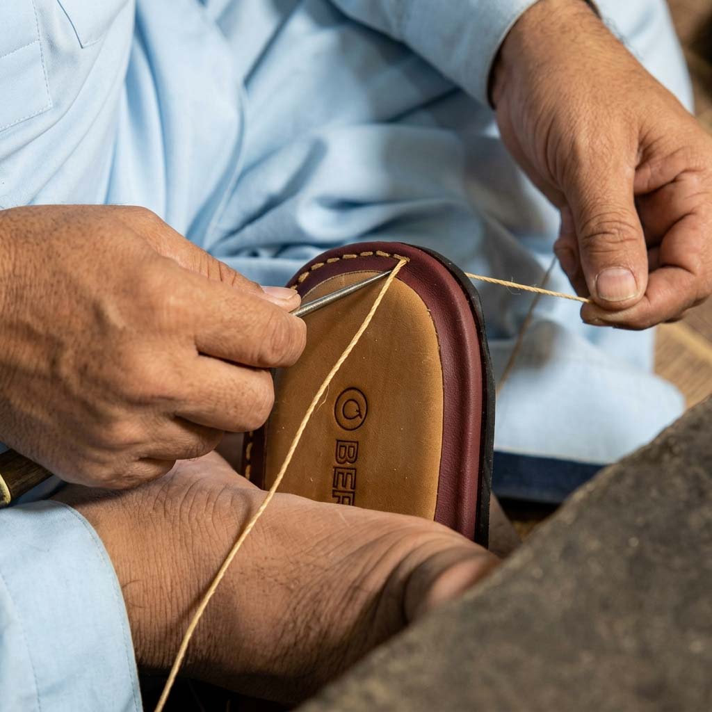 Close-up of a master artisan meticulously hand-stitching the premium leather edge of a Bera luxury footwear sole using heavy-duty waxed thread.