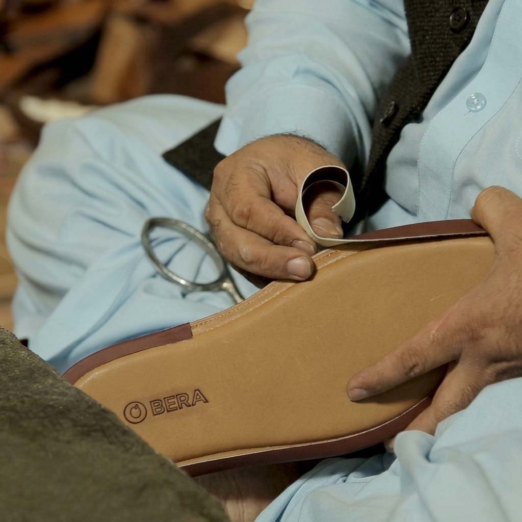 Master craftsman meticulously hand-applying contrasting leather piping around the sole edge of a Bera luxury sandal.