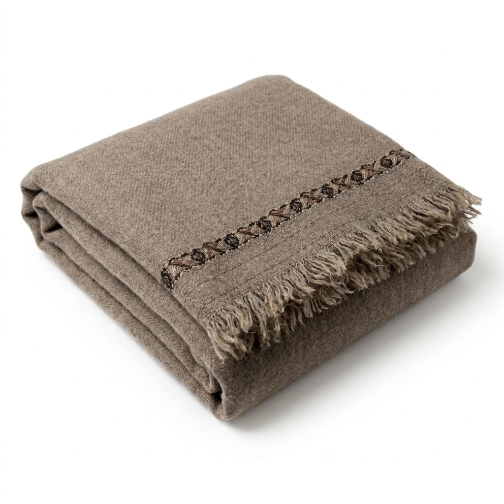 Neatly folded men's dark charcoal brown wool shawl featuring a subtle beige woven geometric border and fringed tassel ends   